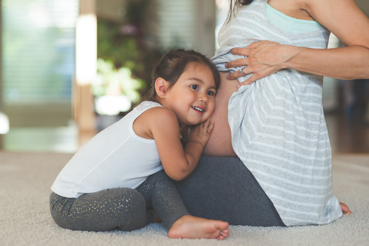 Toddler listening to her mother's pregnant tummy